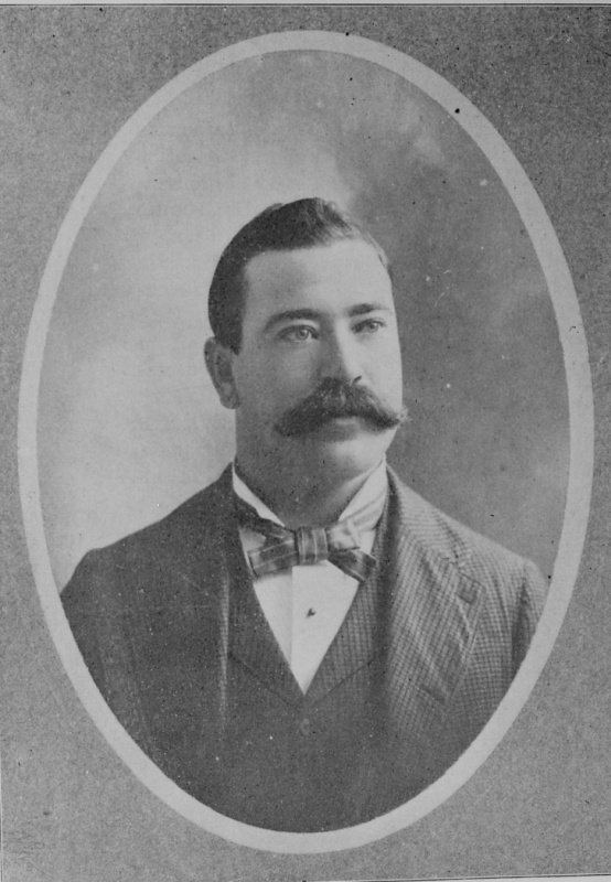Oval half-tone book portrait of a young man with dark hair and a large moustache, wearing a plaid bow tie and a checked jacket.